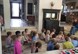 Dzieci siedzą na podłodze w budynku i słuchają opowiadań o koniach.
