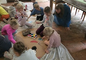 Dzieci siedzą w zespołach i malują farbami ziemniaka z kartonu.