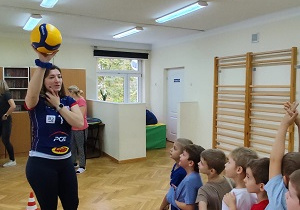 Prowadząca pokazuje dzieciom różne ćwiczenia z piłką.