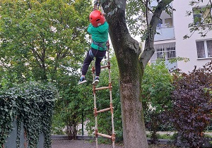 Dziecko w bezpiecznym stroju i asekurowane wspina się po drabince.