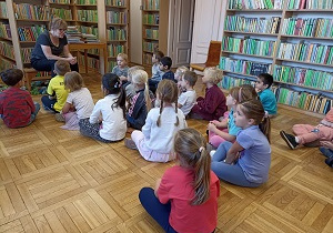 Dzieci siedzą na podłodze i słuchają opowaidania Pani Ewy z biblioteki