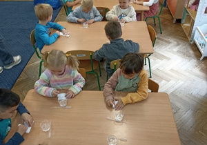 Dzieci siedzą przy stołach i przeprowadzają eksperymenty naukowe.