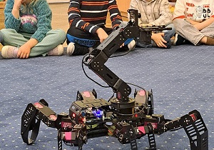 Dzieci siedzą w kole na dywanie, prowadzący prezentuje możliwości robota