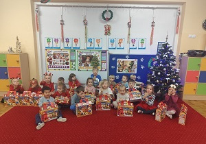 Dzieci siedzą z prezentami przy choince