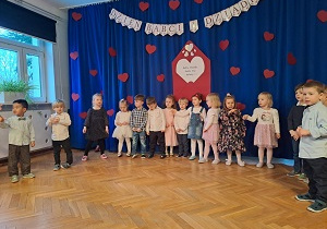 Dzieci stoją w półkolu na scenie. Za nimi dekoracja.