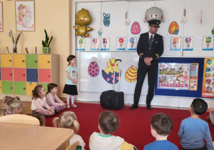 Pan Kapitan stoi przed dziećmi i prezentuje strój pilota